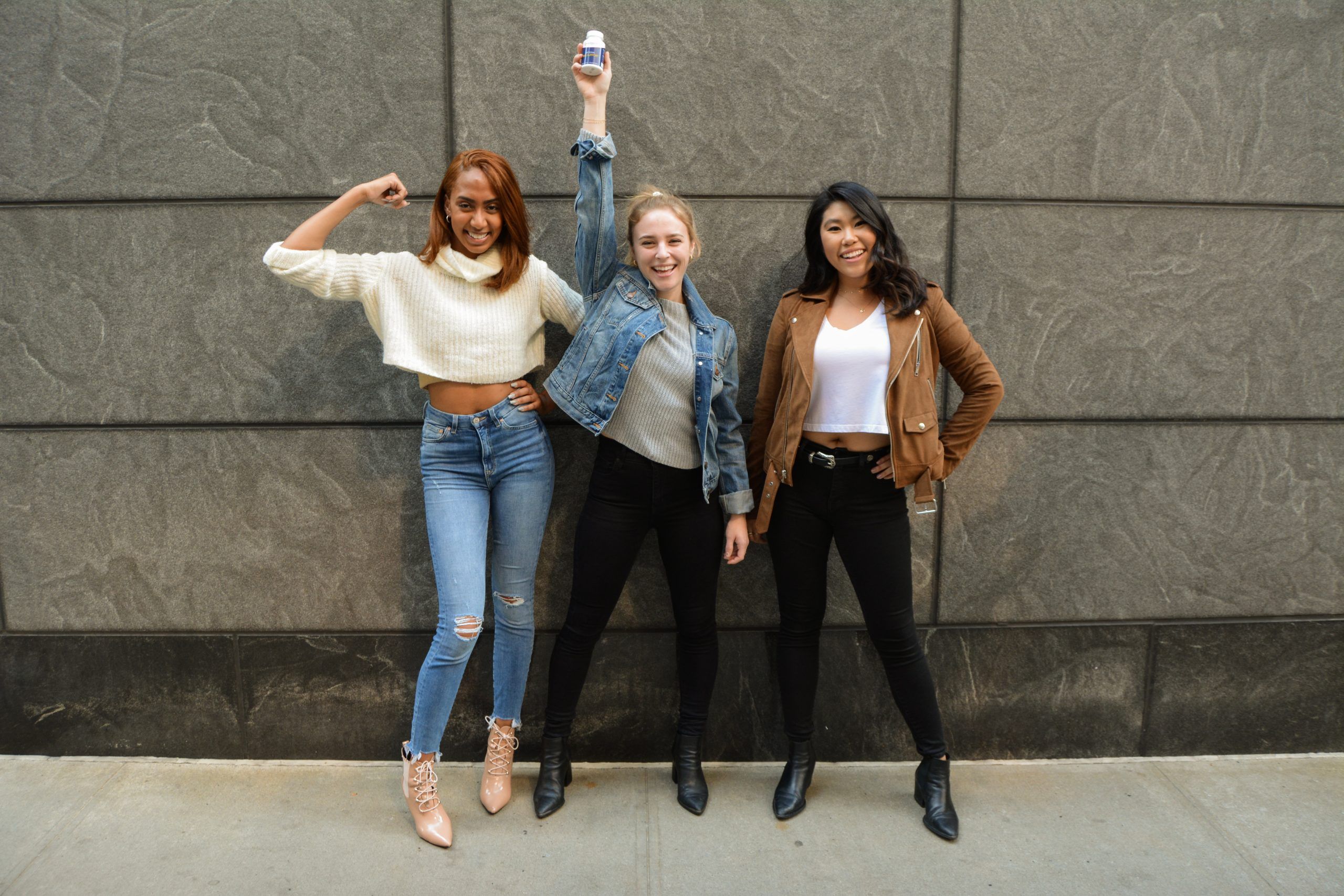 3 Women standing by a wall holding Jubilance PMS Relief Bottle