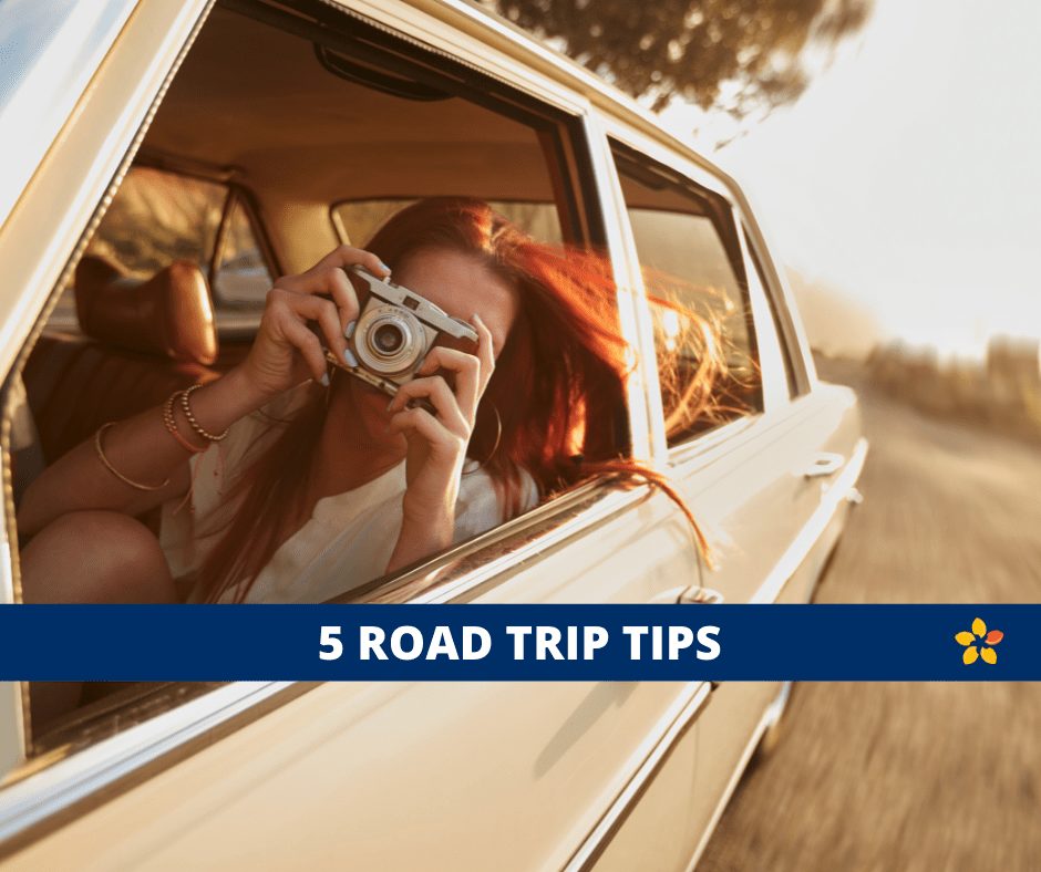 A woman leans out of a car window taking a picture with an old camera for this article on road trip tips.