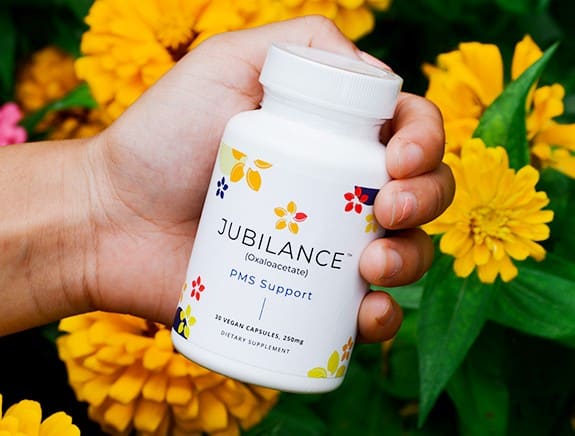 A hand holding a bottle of Jubilance PMS support