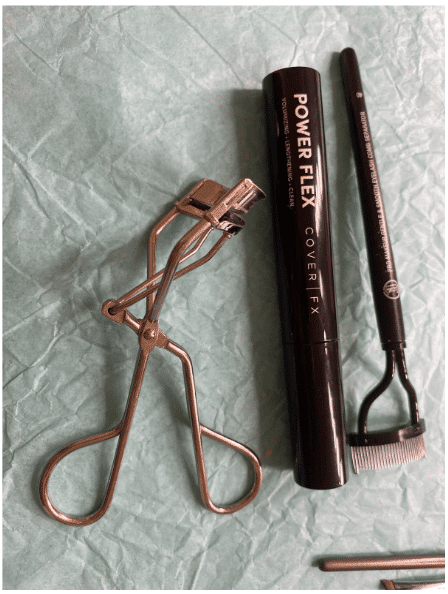 An eyelash curler and mascara sit on a table to use in the summer makeup tutorial.