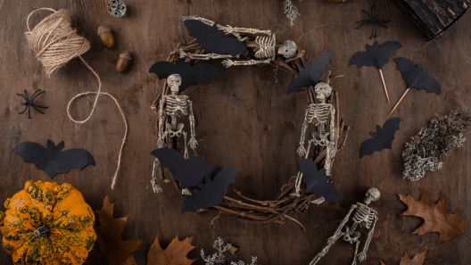A homemade wreath made out of small fake skeletons sits on a table with bat silhouettes, string, and leaves around it.