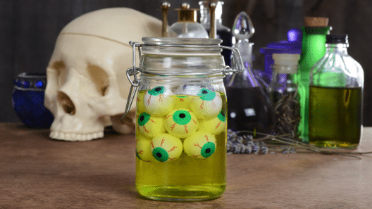 A glass jar with water changed by food coloring in it, also has fake eyeballs floating in the water.
